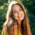 Woman with long brown hair smiling outdoors with a blurred green background